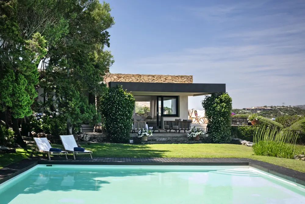 The pool of Villa Clelia set in greenery, with sun loungers and the villa behind
